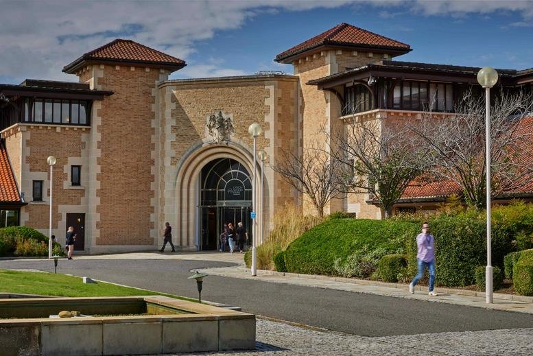 Grand stone exterior and arched entrance of Lynch Wood Park, Peterborough under a blue sky.