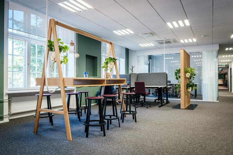 Spacious coworking area with high wooden desk, stools, and indoor plants at Maakri Tänav 19-21.