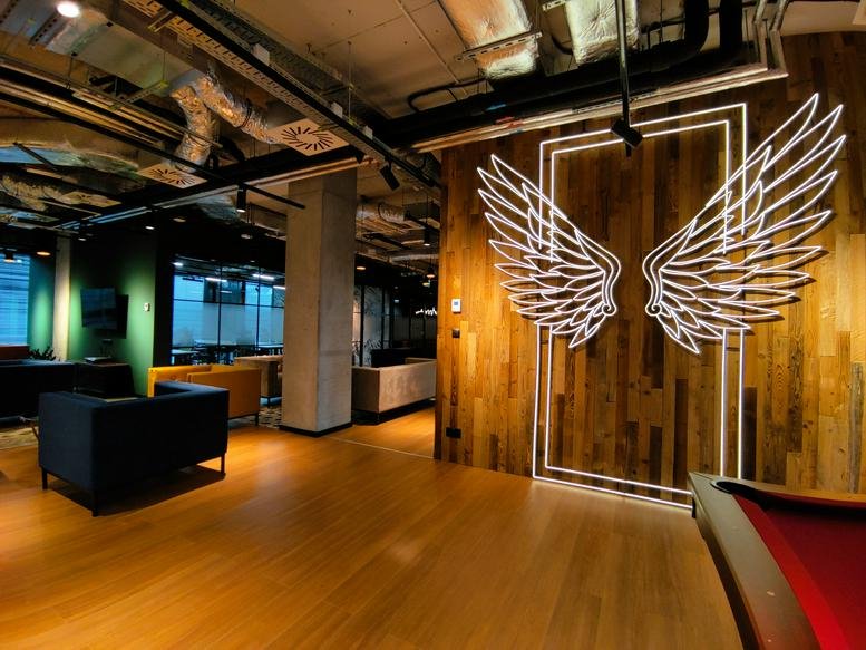 Breakout area at MARCINA KASPRZAKA 4 featuring wood-paneled walls and glowing neon wing art.