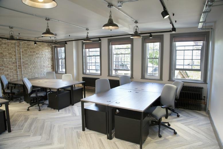 Spacious open-plan workspace with multiple desks, industrial lighting, and large windows.