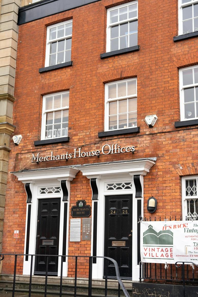 Exterior facade of Merchants House showing red brick walls and black double-door entrances.