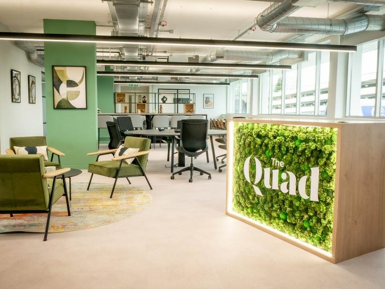 Reception area featuring a wooden desk with a green living moss wall and branded signage.