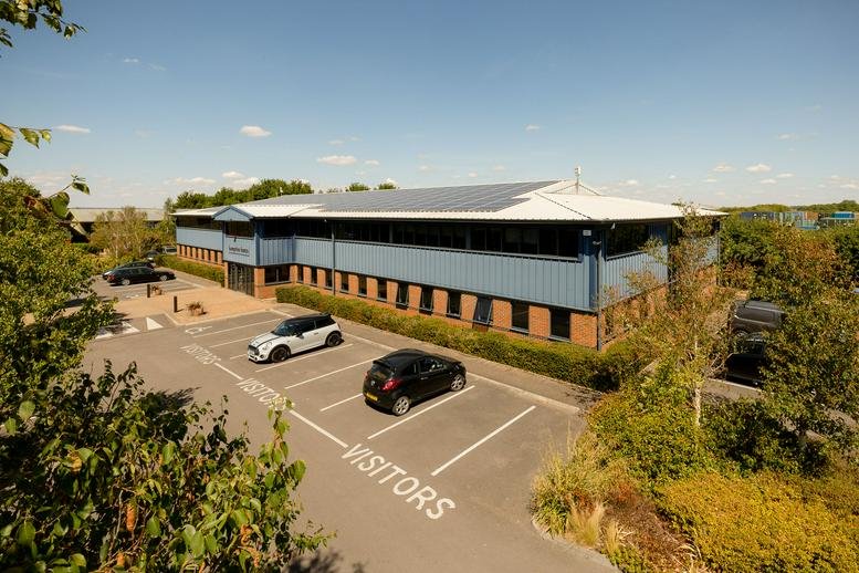 Elevated view of the two-story blue and brick office building facade and visitor parking lot.