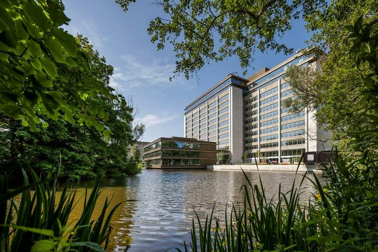 Exterior view of the modern glass-facade Rembrandt Park building situated by a lake.