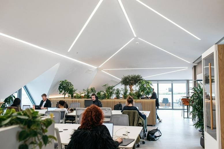 Modern coworking lounge featuring geometric ceiling lights and lush indoor greenery.