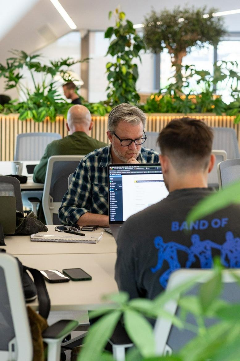 Bright open-plan workspace featuring long white desks and indoor trees.