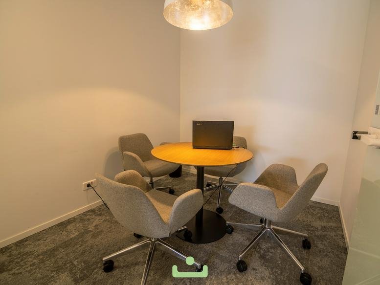 Small private meeting room with four grey chairs and a round wooden table.