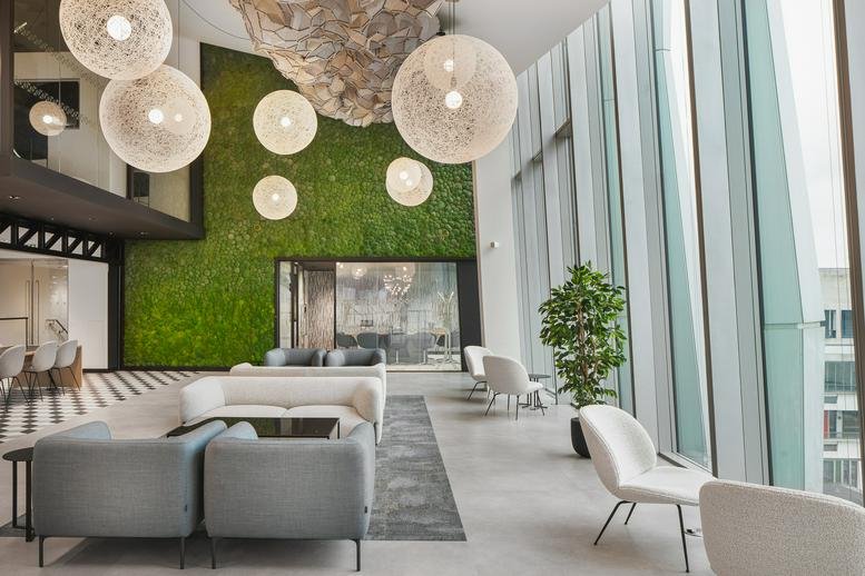 Bright communal lounge featuring a green moss feature wall, grey sofas, and oversized spherical pendant lights.