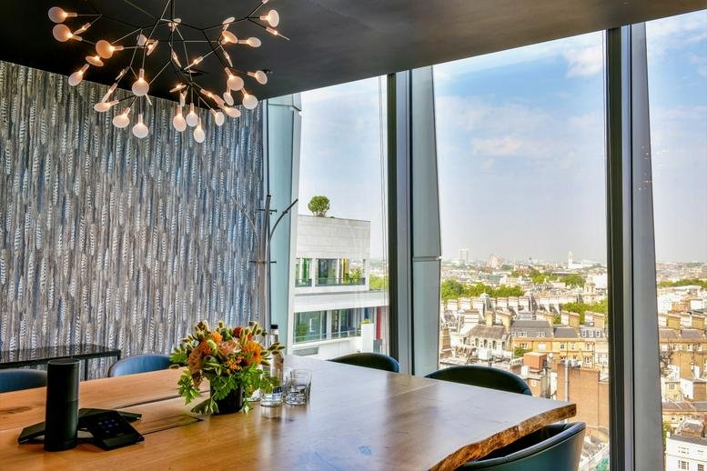 Bright conference room with a natural wood table, plant centerpiece, and panoramic skyline view.
