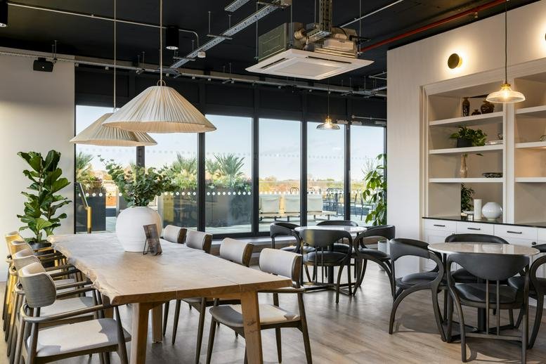 Spacious communal dining area with long wooden tables, potted plants, and floor-to-ceiling windows.