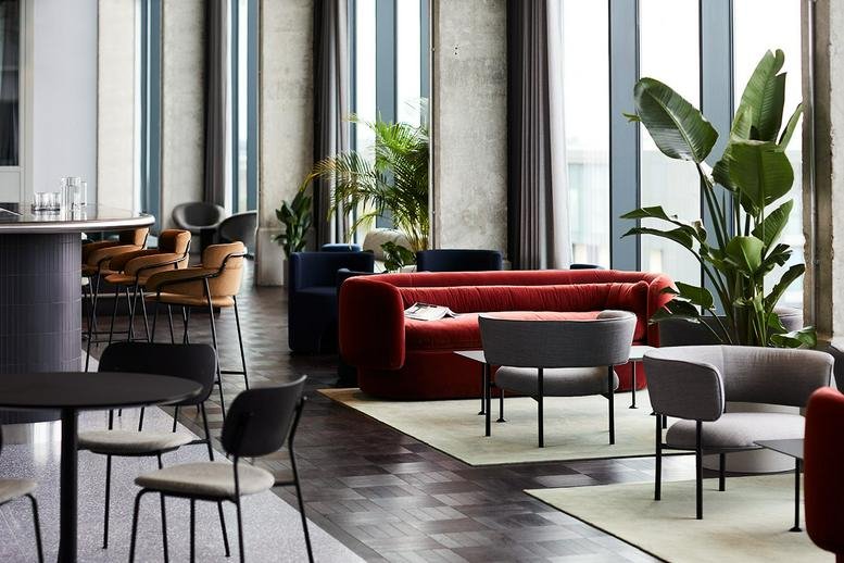 Spacious lounge area with a plush red sofa, grey armchairs, and floor-to-ceiling windows.