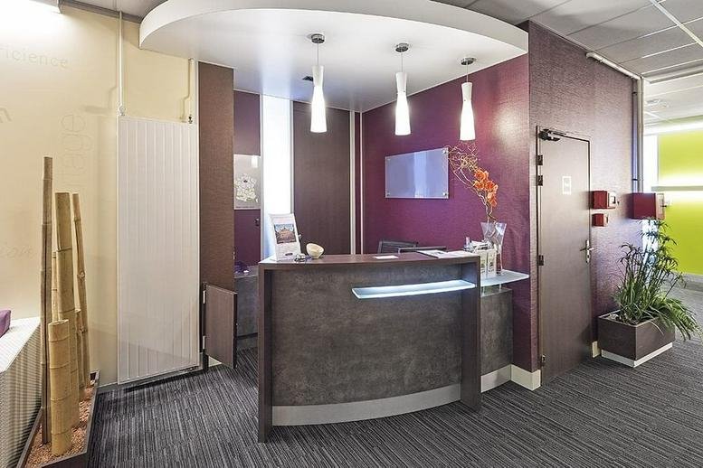 Modern reception area at 1 Rue Du Guesclin featuring a curved dark wood desk and purple accent walls.