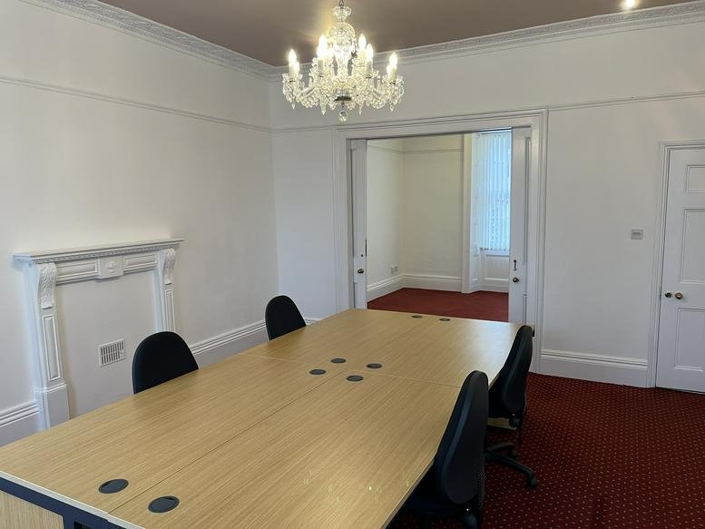 Bright meeting room with a wooden table, chandelier, and a white decorative fireplace.