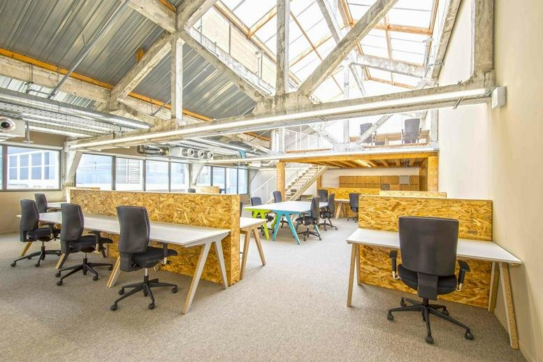 Spacious sunlit open workspace at Les Halles de la Cartoucherie with industrial skylights and wooden desks.