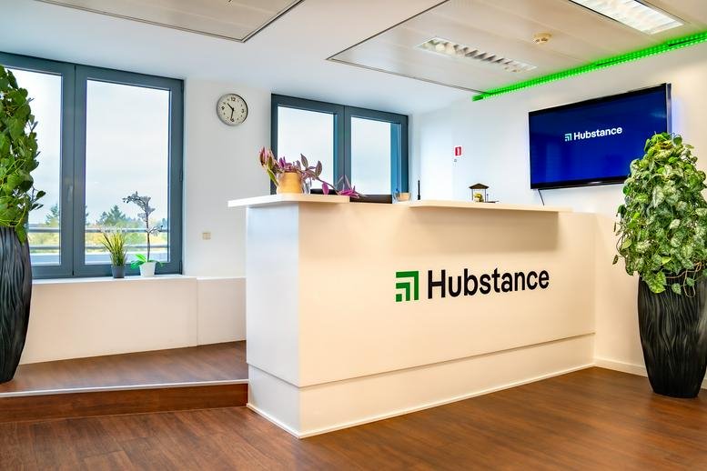 Bright reception area with a white branded desk, wooden floors, and indoor plants.