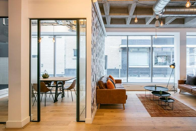 Spacious communal lounge at 114-116 Curtain Road, The Desk with leather sofas and industrial ceilings.