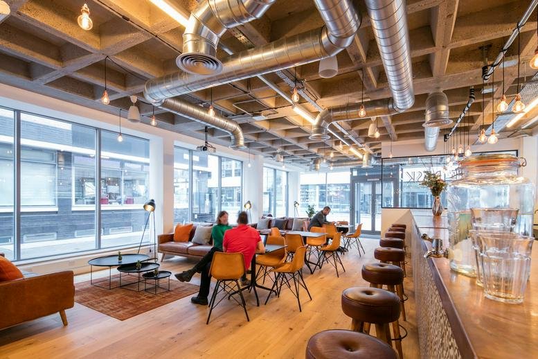 Spacious communal lounge at 114-116 Curtain Road, The Desk, featuring industrial ceilings and a bar area.