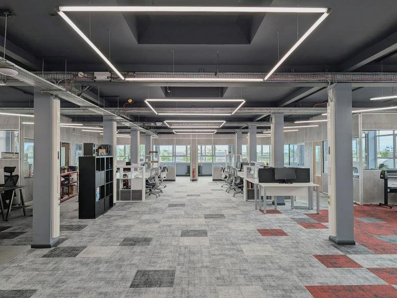 Spacious open-plan workspace at Leigh Works with modern square overhead lighting and carpeted floors.