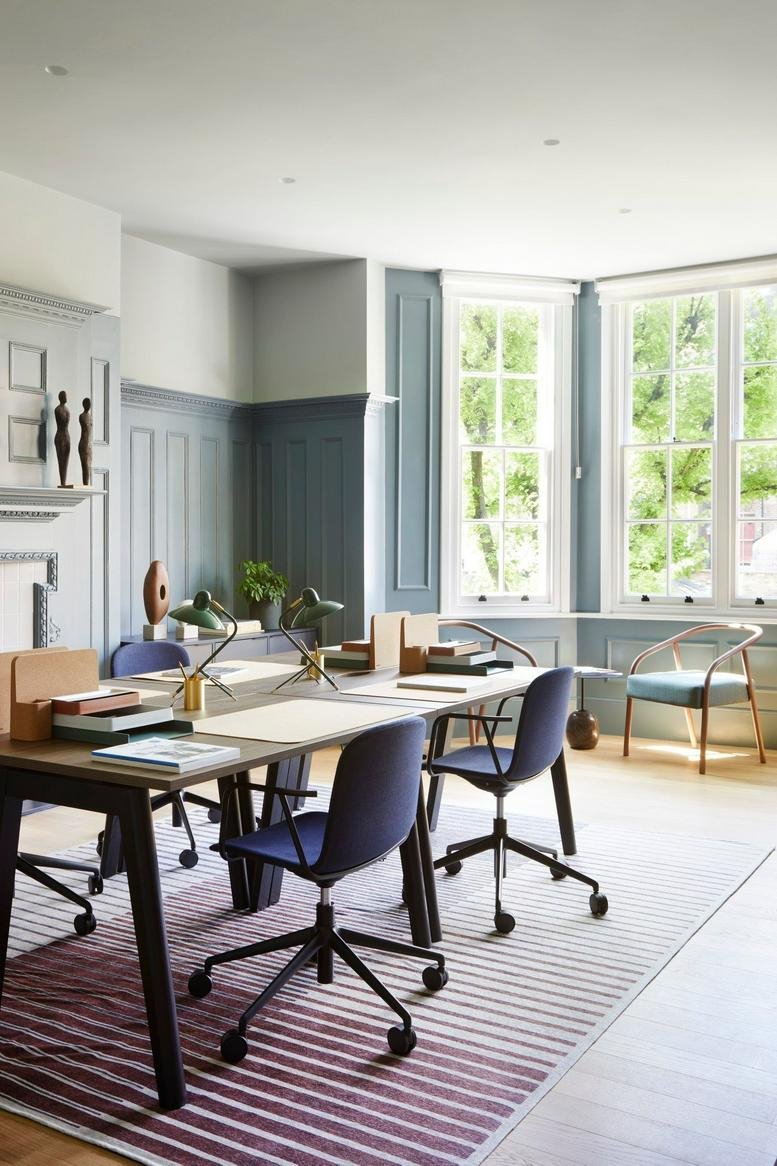 Spacious office featuring a striped rug, blue chairs, and large windows overlooking trees.