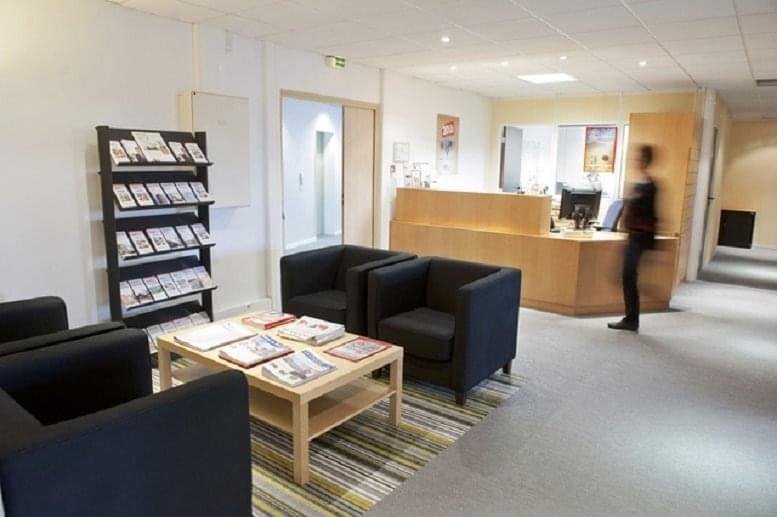 Bright reception area with a wooden front desk, black armchairs, and a magazine rack.