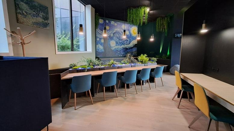 Modern coworking space with a long wooden table, blue velvet chairs, and a starry night mural.