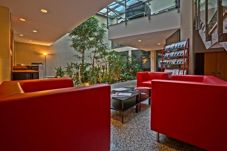 Lobby at 120 rue Jean Jaures with red armchairs and an internal garden under a glass ceiling.