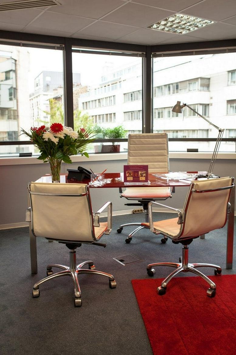 Private office suite at 121 Rue d'Aguesseau featuring a wood desk, white leather chairs, and city views.