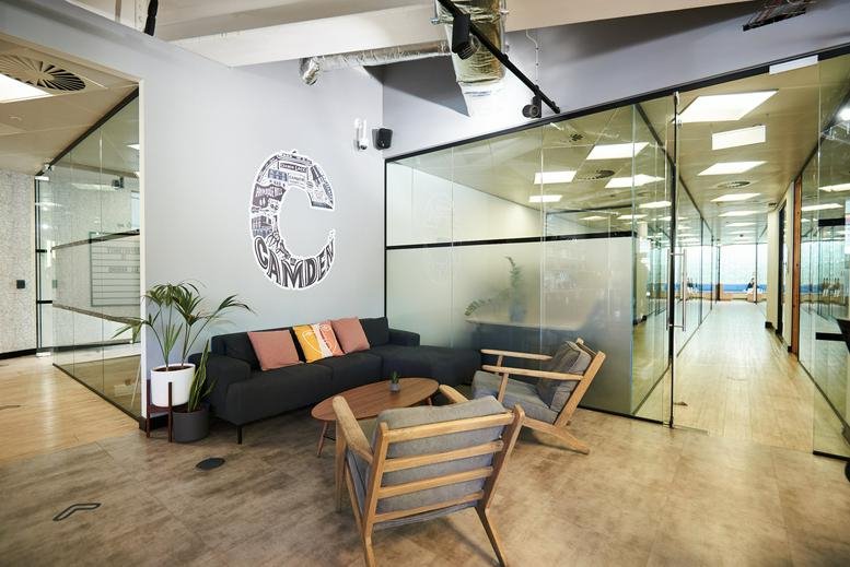 Spacious reception lounge at 13 Hawley Crescent, Camden, with a dark sofa and glass-walled corridors.