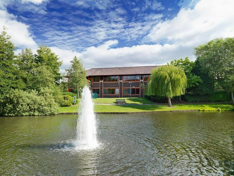 Exterior view of the brick facade of 130 Aztec West reflected in a peaceful pond with a fountain.