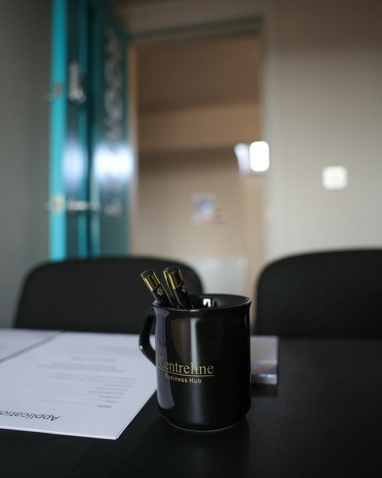 Close-up of a desk with a branded mug holding pens and paper.