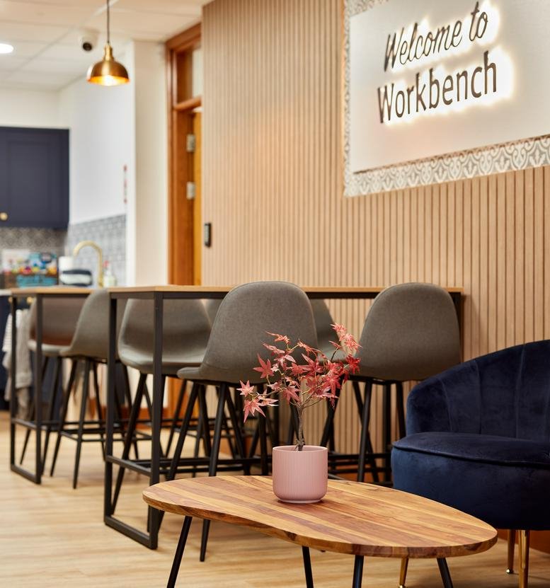 Reception and breakout area with high tables, wooden accents, and Welcome to Workbench signage.