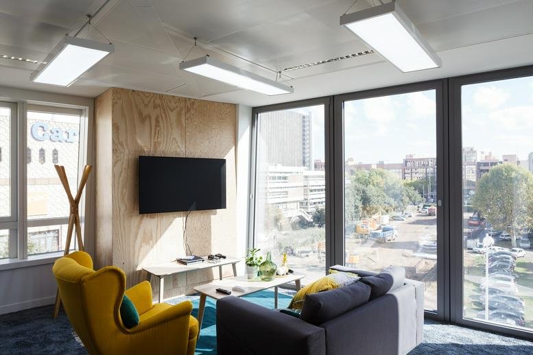 Bright breakout lounge with a yellow armchair and city views at 15, rue des Cuirassiers.