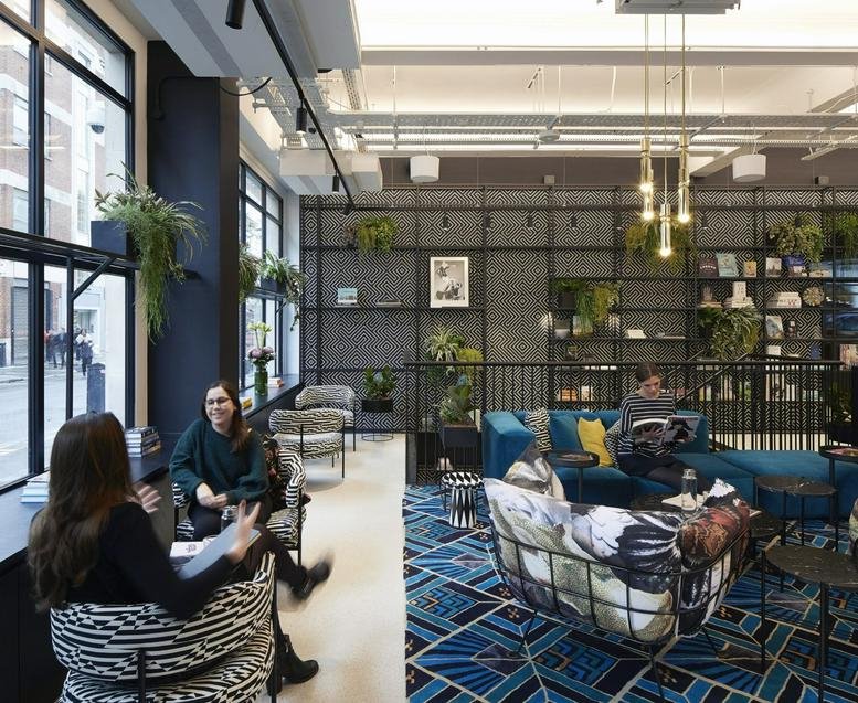 Bright communal lounge with blue patterned rugs, eclectic seating, and a library wall.
