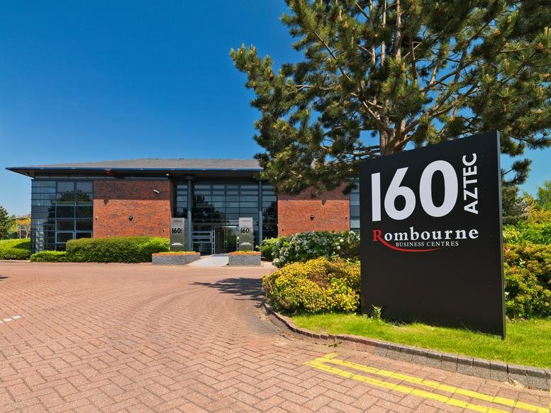 The brick and glass exterior facade of the 160 Aztec office building under a clear blue sky.