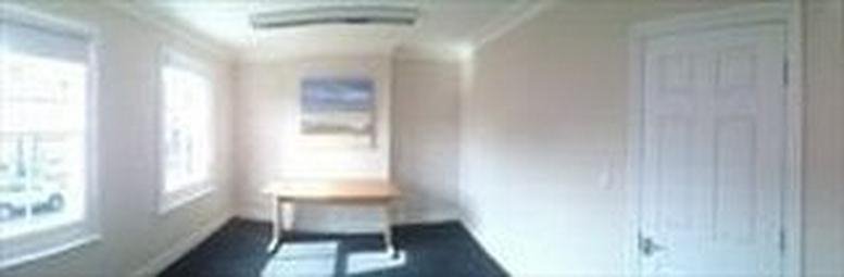 Bright private office featuring a wooden desk and two large windows.