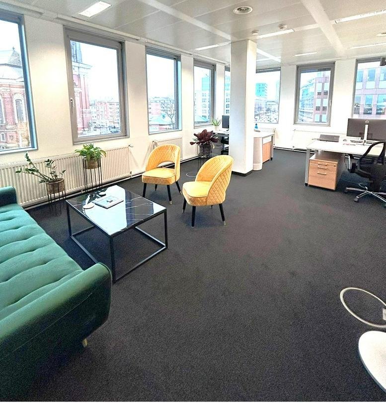 Spacious communal lounge with velvet green sofa and yellow armchairs by large windows.