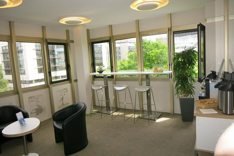 Bright common area at 2 Rue Crucy with window-side breakfast bar, tall stools, and indoor plants.