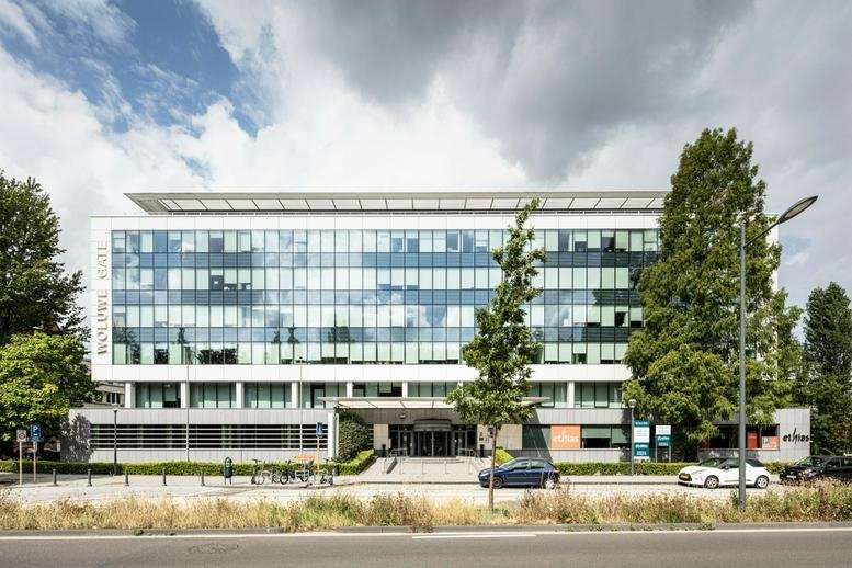 Street view of a modern office building with trees and parked cars.
