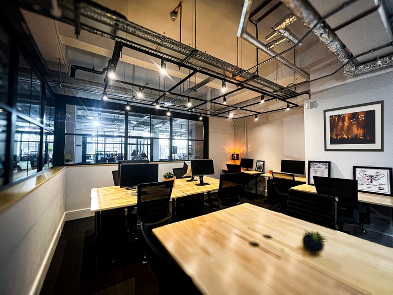 Modern industrial workspace with wooden desks and exposed ceiling pipes.