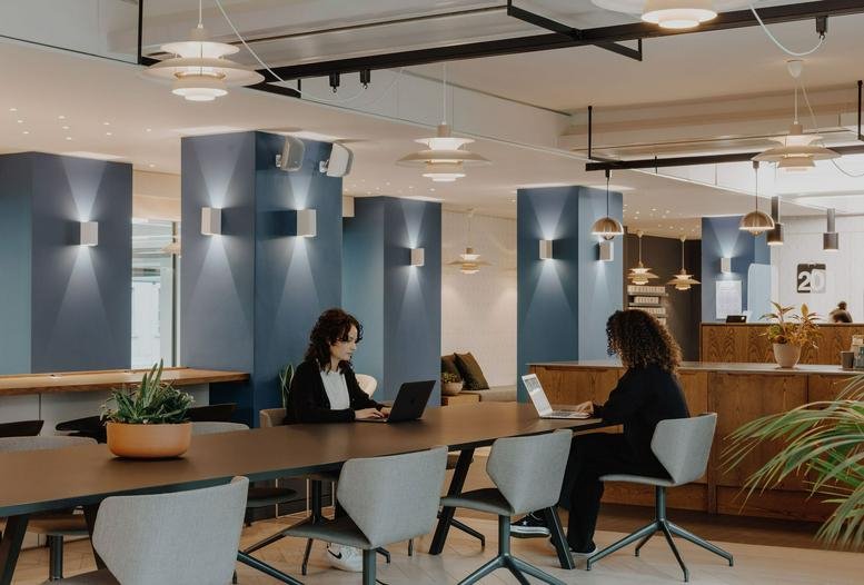Bright coworking area with long wooden tables, blue pillars, and stylish pendant lighting.