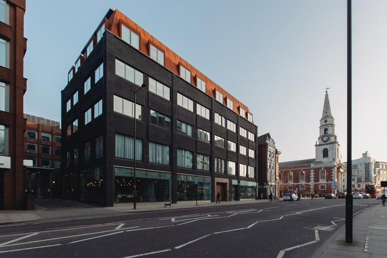Exterior view of the dark brick facade of 201 Borough High Street near a church spire.