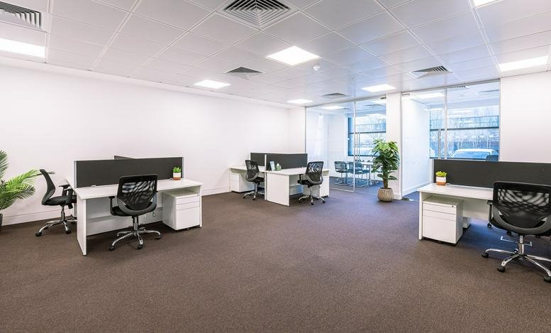 Bright open-plan office space with white desks and black ergonomic chairs.