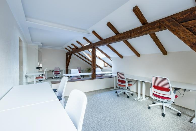 Spacious attic office at Maccollab featuring wooden ceiling beams and rows of white workstations.