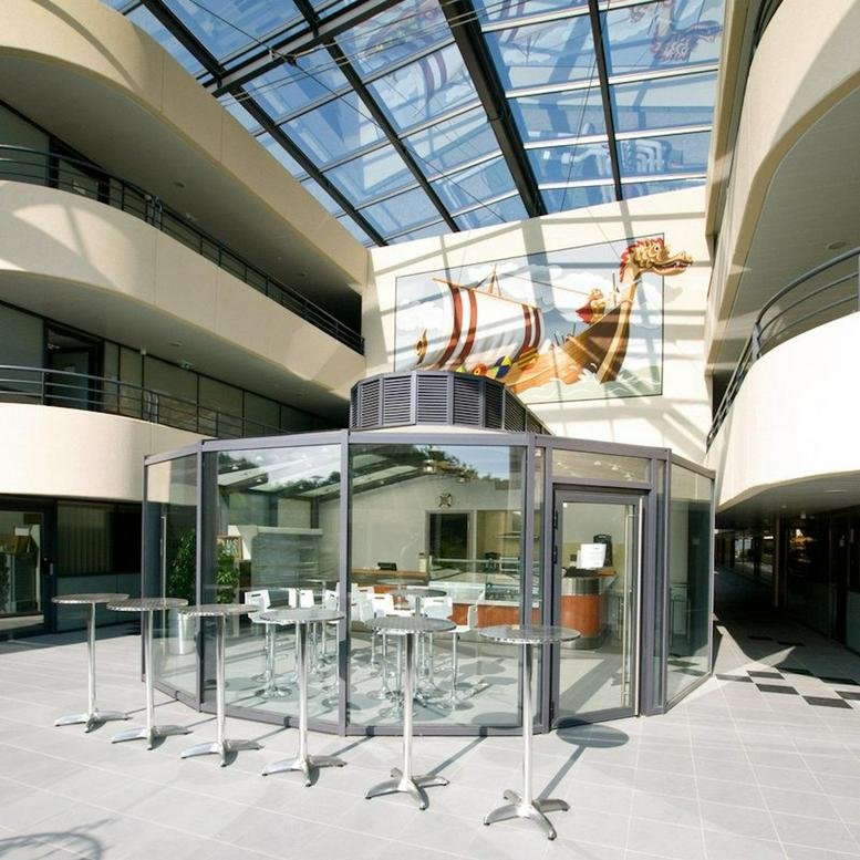 Lobby and central courtyard at 2405 Route des Dolines with glass ceiling and circular cafe kiosk.