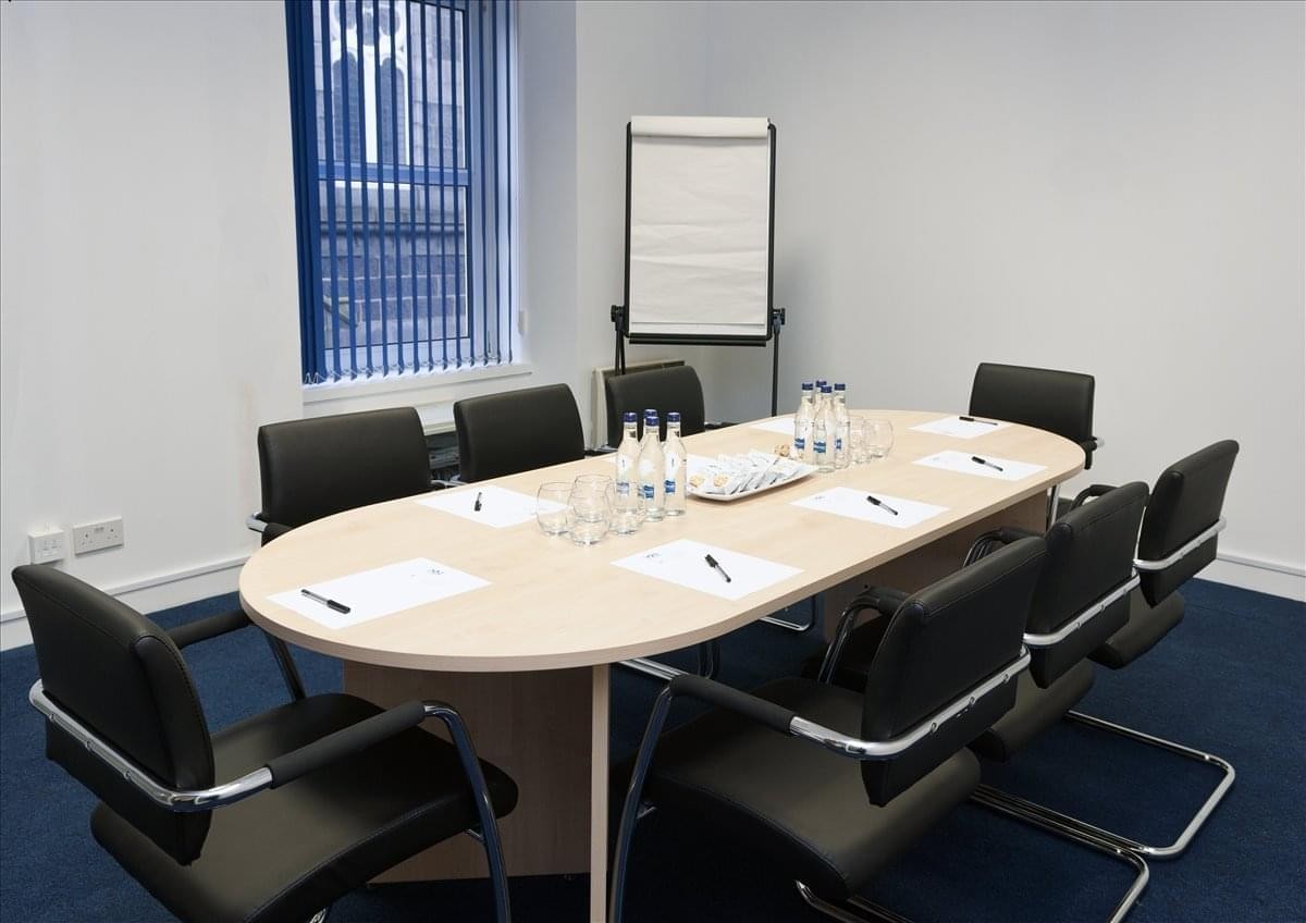 Meeting room at 27 Crown Terrace featuring an oval table, black chairs, and a flipchart.