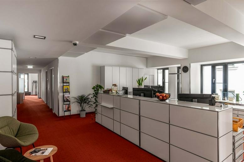 Spacious reception area with a long white counter, red carpeting, and indoor plants.