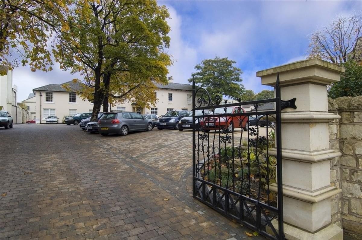 Cobbled courtyard entrance featuring a black iron gate and a white building in the background.