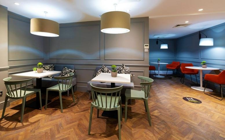 Spacious dining and breakout area with green chairs and wooden herringbone floors.