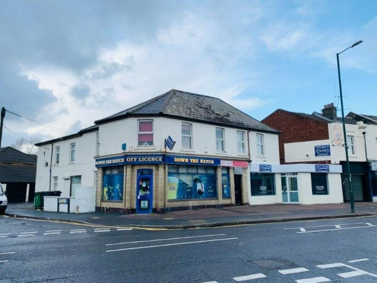 Exterior view of the white corner building at 303 Holdenhurst Road featuring shopfronts.