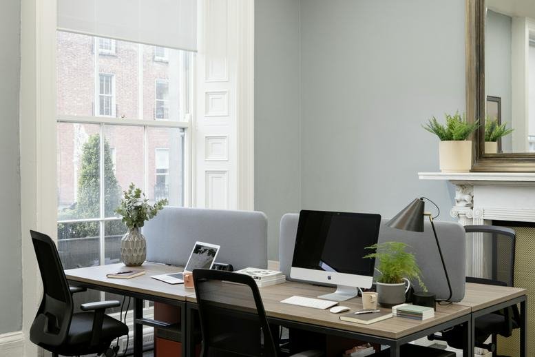 Spacious sunlit office with wooden desks and large windows.